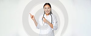 Smiling asian doctor, female healthcare worker pointing at upper left corner, looking amazed, showing medical