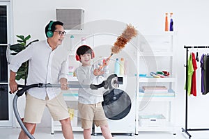 Smiling Asian father and little boy child is enjoying for House cleaning together in Laundry room. They listen to music by