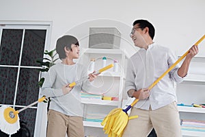 Smiling Asian father and little boy child is enjoying for House cleaning together in Laundry room. They singing with mop for play