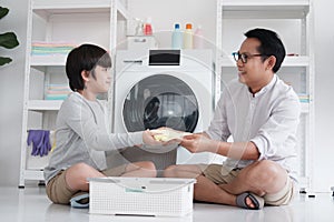 Smiling Asian father and little boy child is enjoying and Washing clothes together in Laundry room on holiday. Family activities