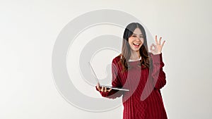 A smiling Asian female college student is holding a laptop and showing the Okay hand sign