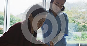 Smiling asian female doctor helping senior female patient to walk using walking frame