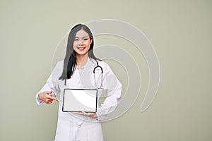 Smiling Asian female doctor showing tablet, standing against grey background