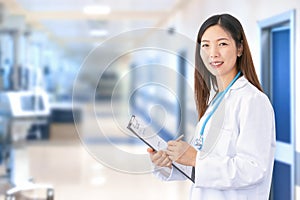 Smiling Asian female doctor wearing lab coat and stethoscope as she writes a document in her folder