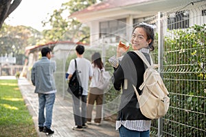 A smiling Asian female student is walking on a footpath on her campus, going to school