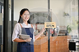 Smiling Asian female waitres stands at the front door with a digital tablet in her hand