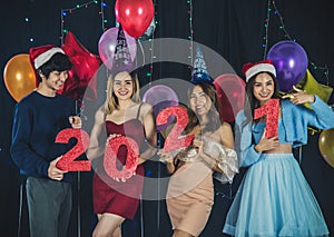 Smiling asian friends having fun celebrating on Christmas and New Year Party holding red shiny paper numeral 2021