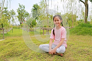 Smiling Asian girl child looking camera while sitting on lawn in the garden