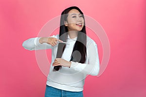 Smiling asian girl combing long strong hair, getting ready for date. Happy young stylish woman enjoying beauty routine