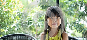 Smiling asian girl sitting on a chair looking at a camera with green background behind. Portrait adorable asian girl with smiling