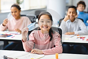 Smiling asian girl taking off disposable medical mask at classroom