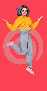 Smiling Asian girl teenager in mid-jump against vibrant red color background. Exuberance and happiness of youth
