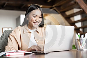 Smiling asian girl waching webinar, having work video call from home, working freelance remotely, looking happy at