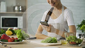 Smiling Asian girl watching video recipe on smartphone before cooking dinner