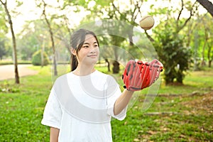 Smiling Asian girl wearing leather glove throwing baseball up into the air