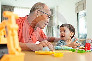 Smiling Asian Grandfather and Grandson playing with plasticine