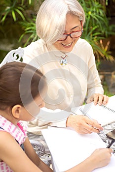 Smiling asian grandmother is drawing outside with granddaughter. Casual, outdoors