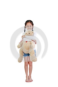 Smiling asian little child girl hugging a teddy bear doll standing isolated on white background