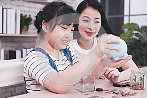 Smiling Asian little asian girl child blue piggy bank for saving money on wooden table. Child educational for homeschool photo