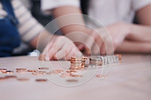 Smiling Asian little asian girl child is counting coins on wwoden table for saving money for the future with mother on wooden