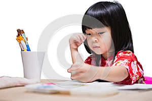 Smiling Asian little girl happily draws with colorful pencils or watercolor in a classroom, embodying the joy of childhood