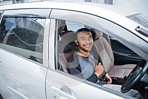 smiling Asian male driver holding seat belt before a drive