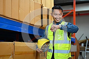 Smiling asian male supervisor checking time on his watch while standing in warehouse