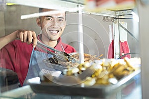 The smiling Asian male waiter takes the fried chicken on the iron tray