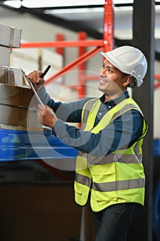 Smiling asian male worker using digital tablet and checking quantity of storage product on shelves full of packed boxes