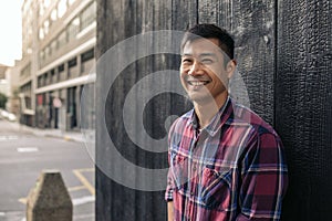 Smiling Asian man leaning against a wall in the city