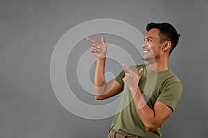 Smiling Asian man pointing his finger aside on an empty space, isolated on a grey background