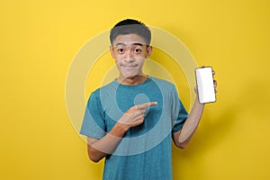 Smiling Asian man showing on empty smartphone screen, pointing at mobile phone and looking satisfied