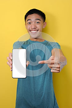 Smiling Asian man showing on empty smartphone screen, pointing at mobile phone and looking satisfied