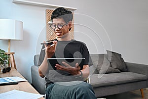 Smiling asian man talking on mobile phone and using digital tablet at home.