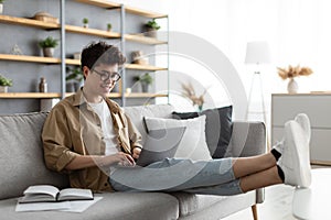 Smiling asian man win glasses orking on laptop at home