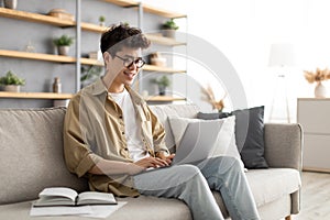 Smiling asian man win glasses orking on laptop at home