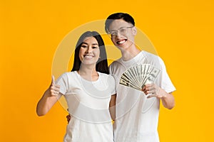 Smiling asian man and woman holding money, showing thumbs up