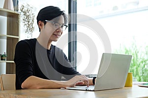 Smiling asian man working with laptop computer at home office