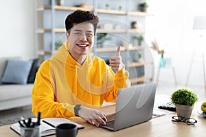 Smiling asian man working on laptop showing thumbs up