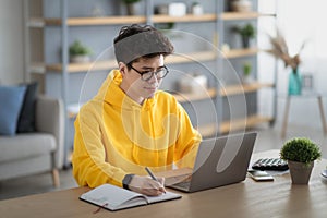 Smiling asian man working on laptop and writing