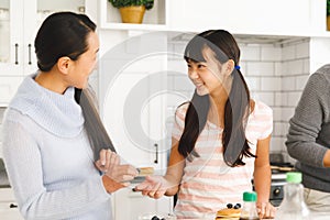 Smiling asian mother and daughter talking while preparing breakfast in kitchen with father