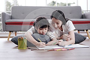 Smiling Asian mother and little asian girl child is drawing and Painting with wooden colored pencils on paper for imagination