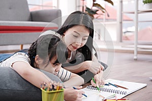 Smiling Asian mother and little asian girl child is drawing and Painting with wooden colored pencils on paper for imagination