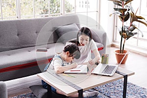 Smiling Asian mother and little girl child is drawing and Painting with wooden colored pencils on paper together in living room.