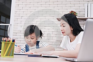 Smiling Asian mother and little girl child is drawing and Painting with wooden colored pencils on paper together in worksapce area