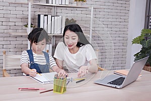 Smiling Asian mother and little girl child is drawing and Painting with wooden colored pencils on paper together in worksapce area