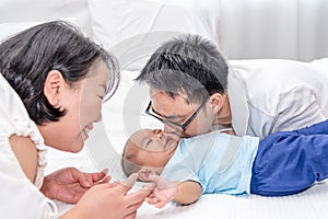 Smiling Asian mother looking at her husband kissing 5 months baby boys son in bedroom