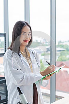 Smiling asian nutritionist doctor woman writing on paper green board in laboratory room