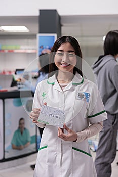 Smiling asian pharmacist holding box of vitamins