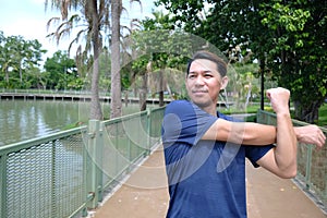 Smiling Asian sportman exercising and stretching his hands for Muscle relaxation and resilient after running and jogging photo